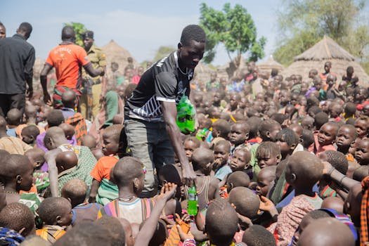 Charity worker distributes beverages to children in an African village, showcasing community support.